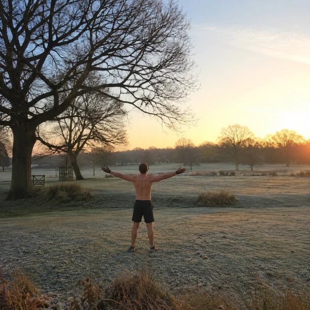 Person standing in Richmond Park near East Sheen with arms outstretched at sunrise, representing an active lifestyle and recovery through rehabilitation