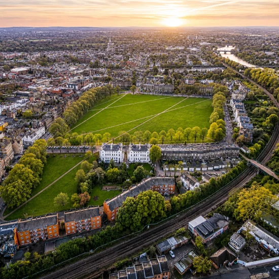 Aerial view of Old Deer Park in Richmond, London, showing the sports grounds, surrounding residential streets, and the River Thames at sunset.